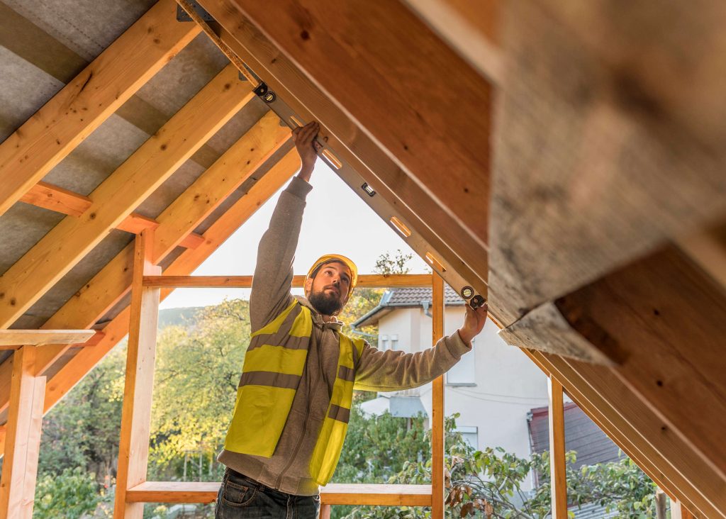 Carpenter wearing a hard hat working on the wooden roof structure of a house.