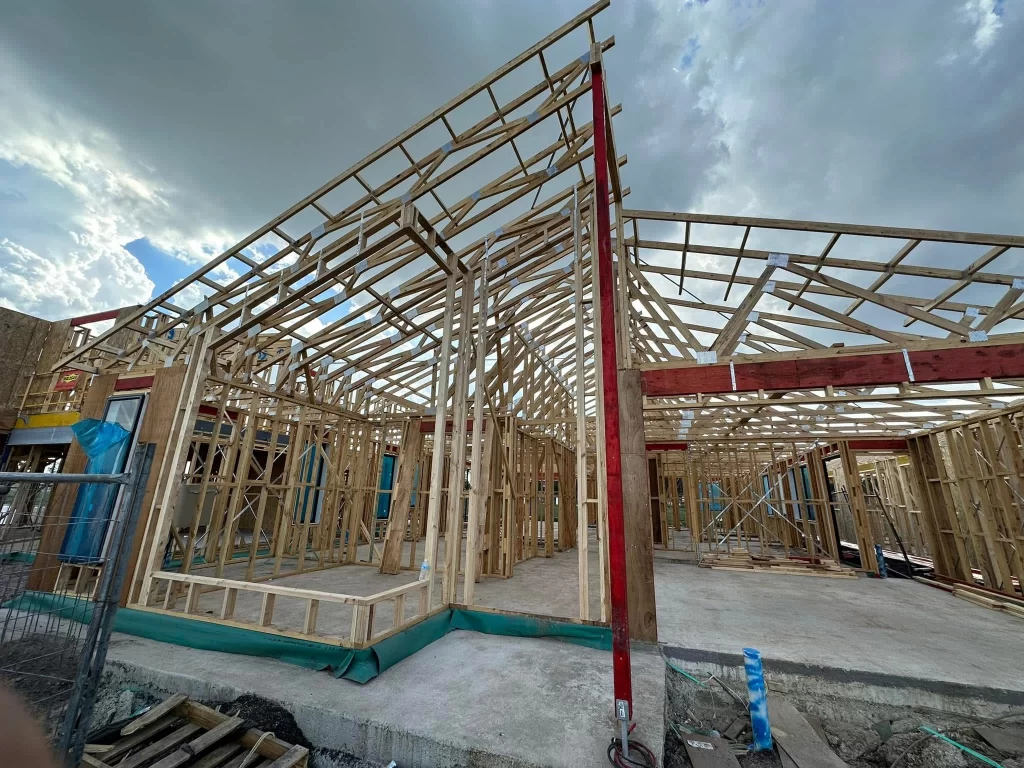 Construction site with partially built wooden house frames and a clear sky in the background.