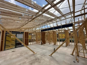 Interior view of a house under construction with wooden framing and partially installed roof trusses.